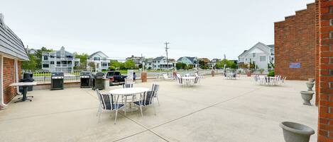 An outdoor patio area with multiple tables and chairs, a barbecue grill, and a brick wall.