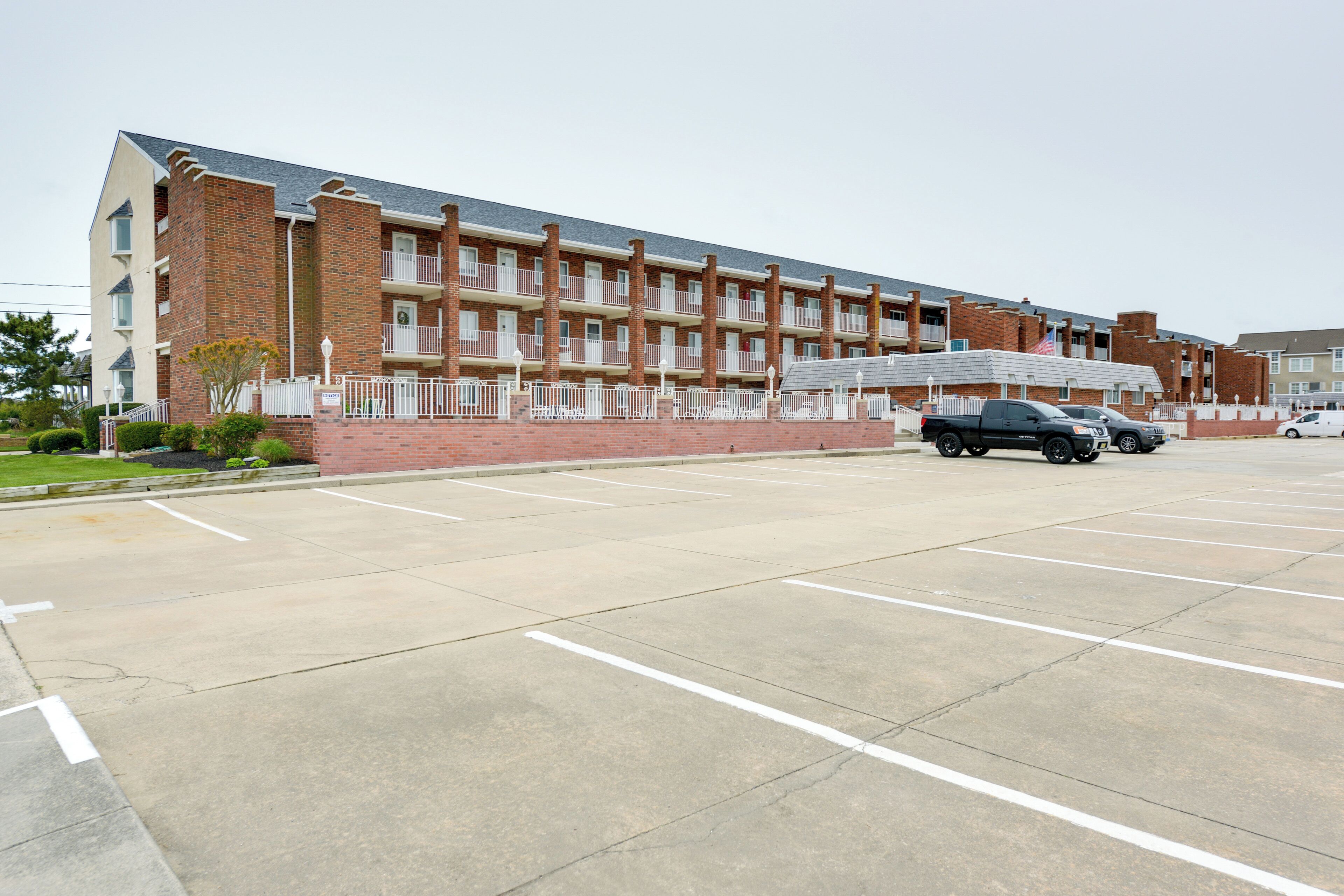 Un immeuble en briques de plusieurs étages, avec un parking situé devant.