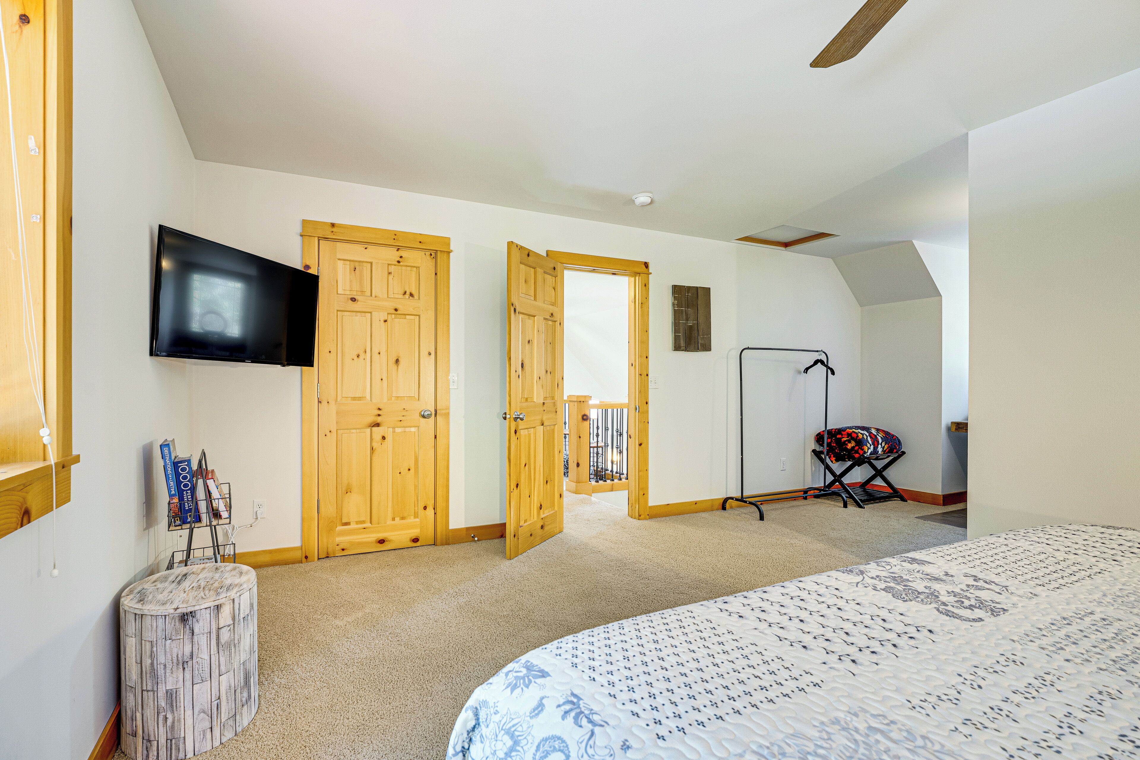 A bedroom with a bed, a television mounted on the wall, wooden doors, a closet, and a small table with items on it.
