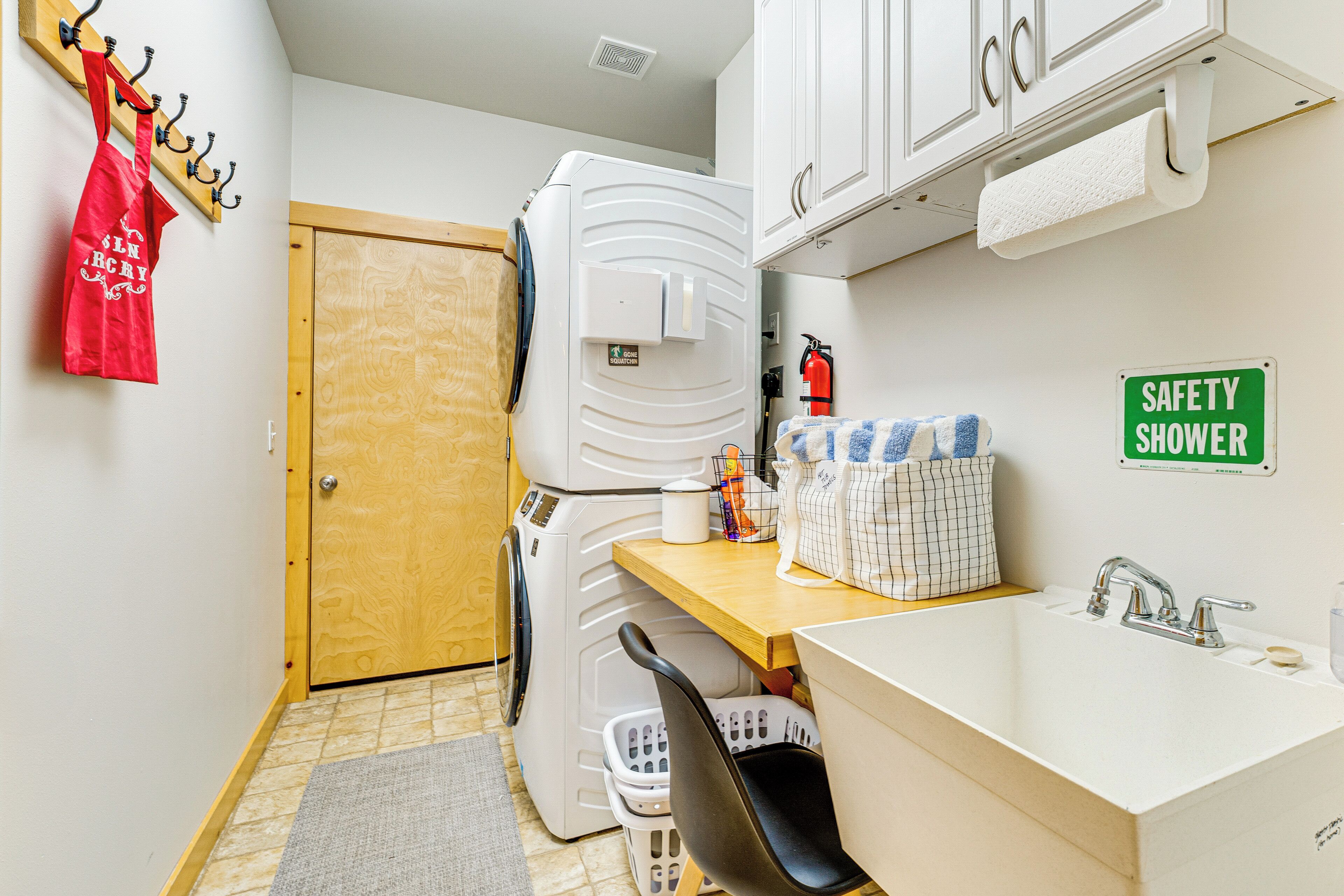 A compact bathroom with a sink, a safety shower sign, a towel dispenser, and a laundry basket.
