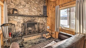 Ein gemütliches Blockhaus-Interieur mit Steinwand, Kamin, Ledersofa und Blick ins Freie.