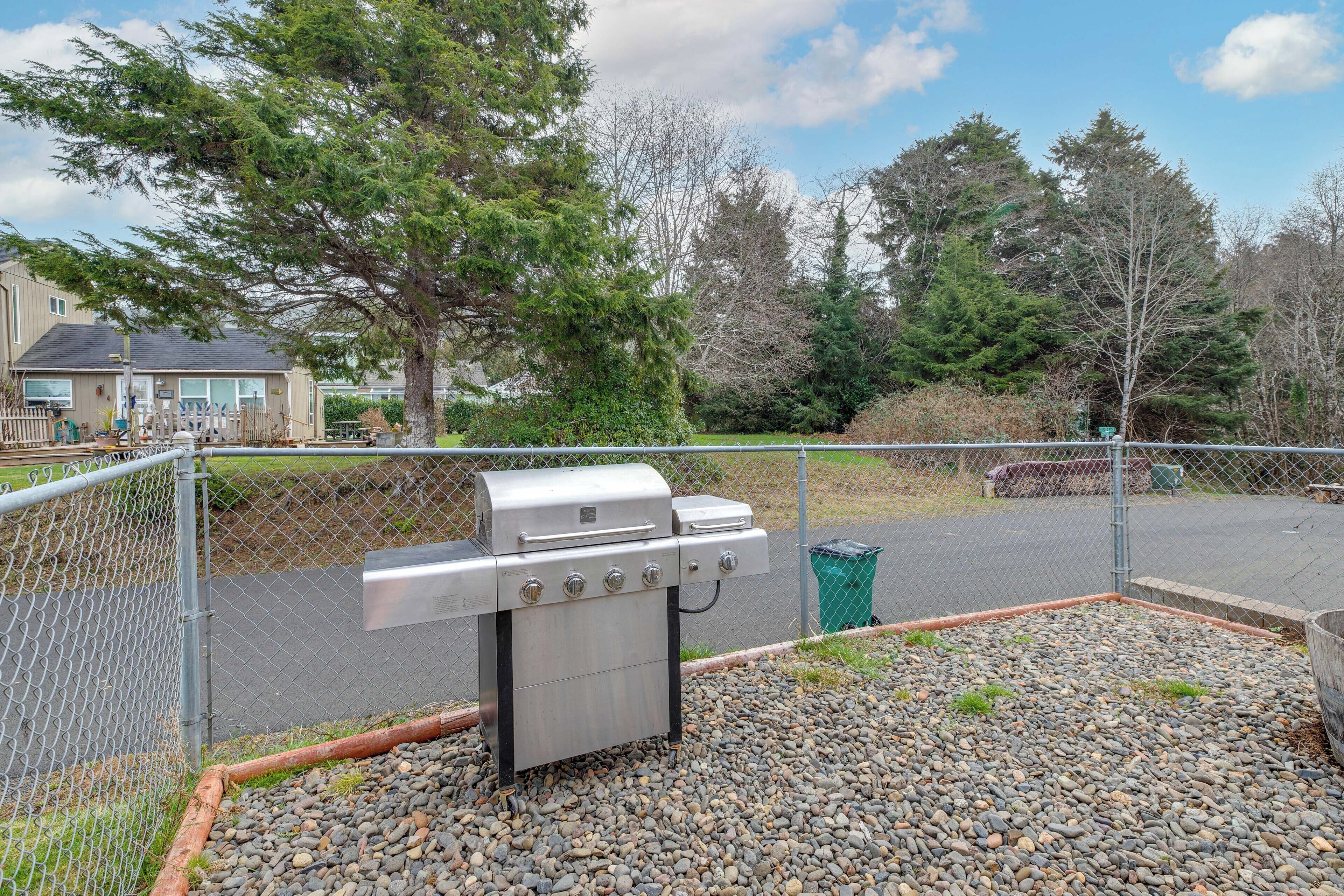 Un barbecue installé dans un espace extérieur clos, avec un sol en gravier, entouré d’arbres et avec un immeuble d’habitation en arrière-plan.