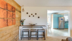 A kitchen with a wooden wall, a white countertop, and three bar stools. There is a refrigerator and blue cabinets in the background. - Rockaway Beach Vacation Rental: Walk to Ocean (Rockaway Beach)