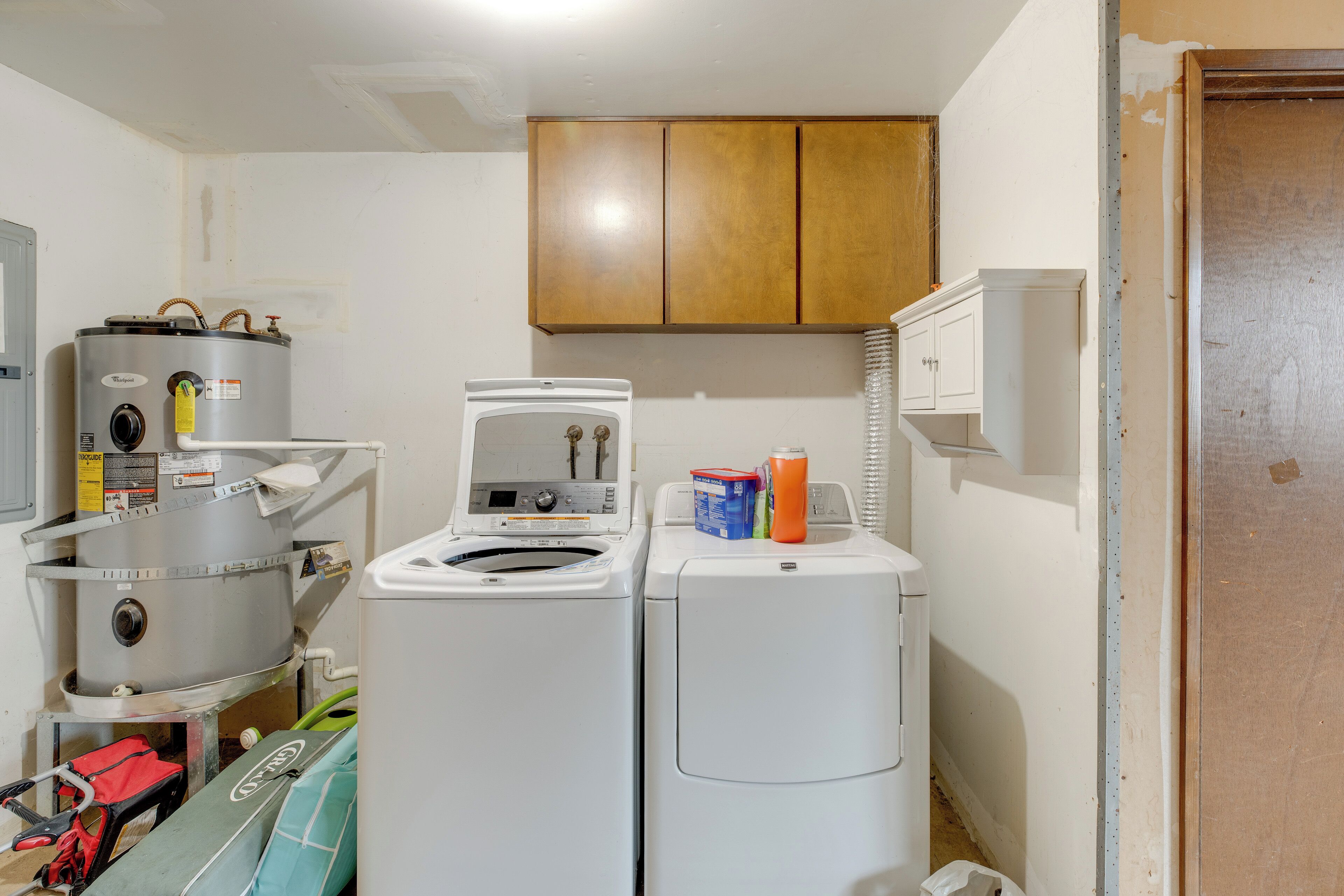 A laundry room with a large industrial washer, a smaller washer, and a dryer. There are cabinets above the appliances and a door to the right.