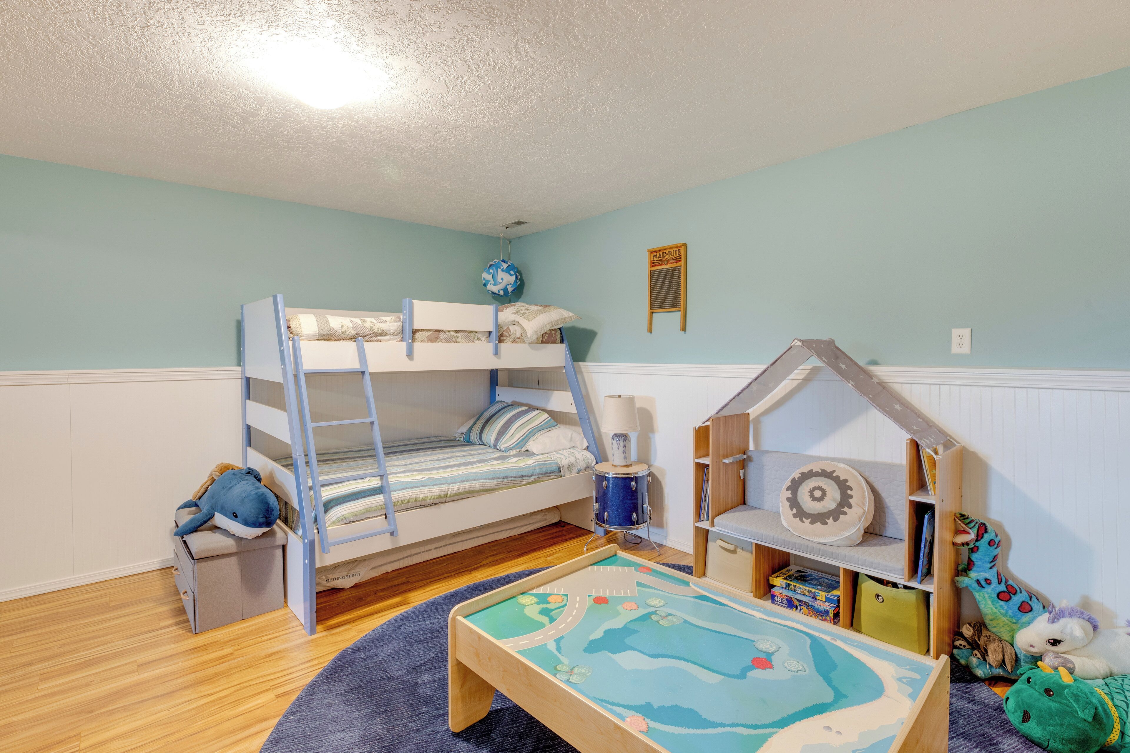 Quarto de criança com beliches, casinha de brincar e uma mesa com estampa de mapa.