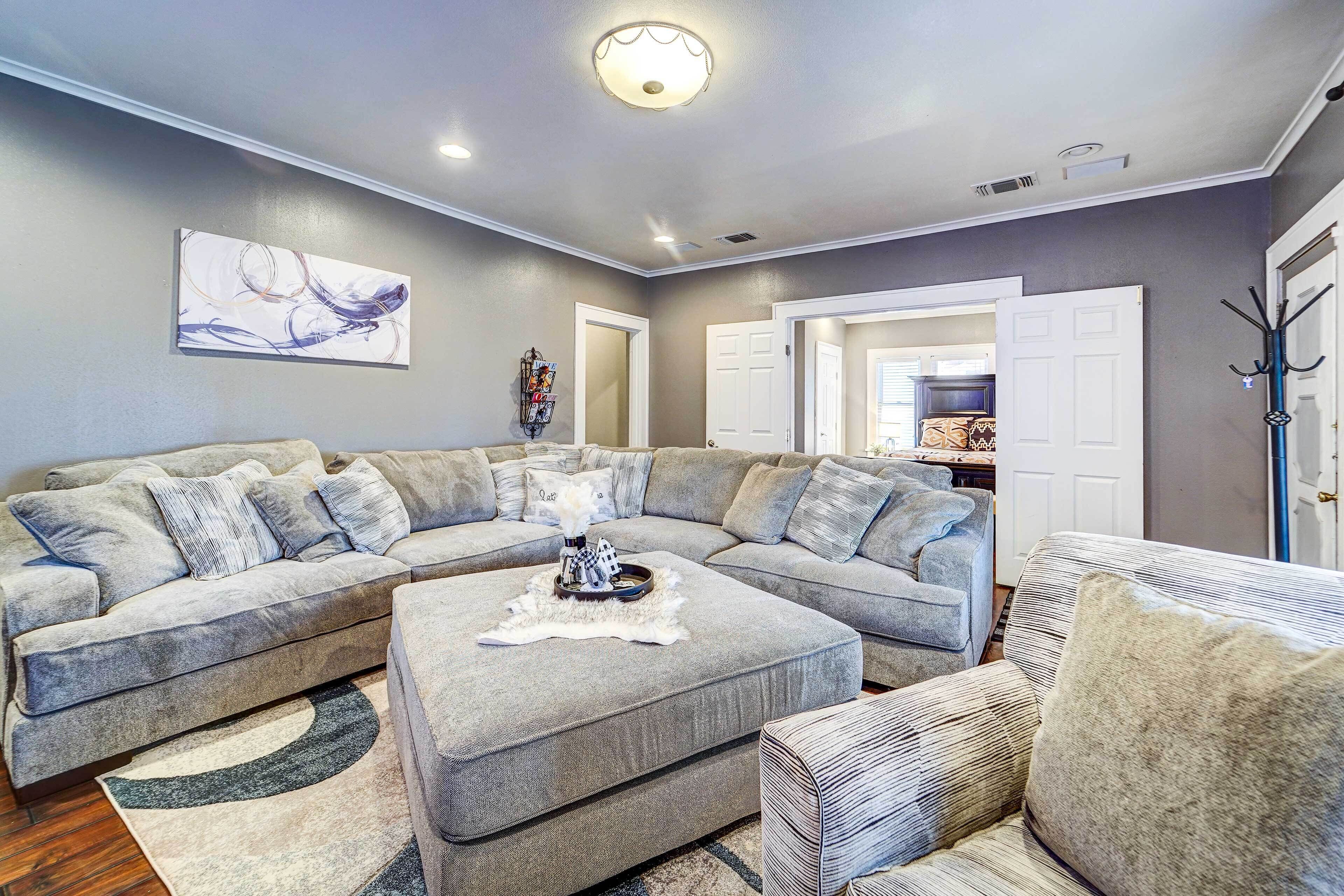 A living room with a sectional sofa, a patterned ottoman, and a rug.