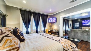 A hotel room with a large bed, a TV mounted on the wall, and a seating area with a sofa and a chair. - By Dtwn Lubbock! Spacious 4BR Home Near Texas Tech (Lubbock)