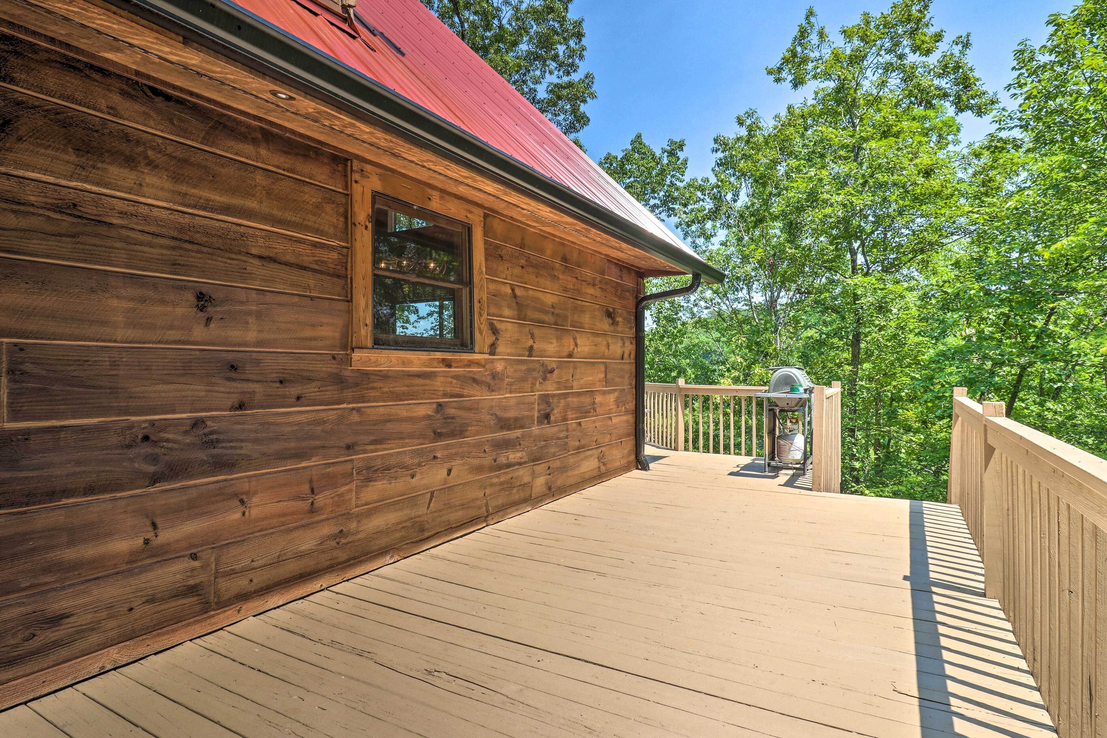 A wooden cabin with a red roof, a deck, and a view of trees.