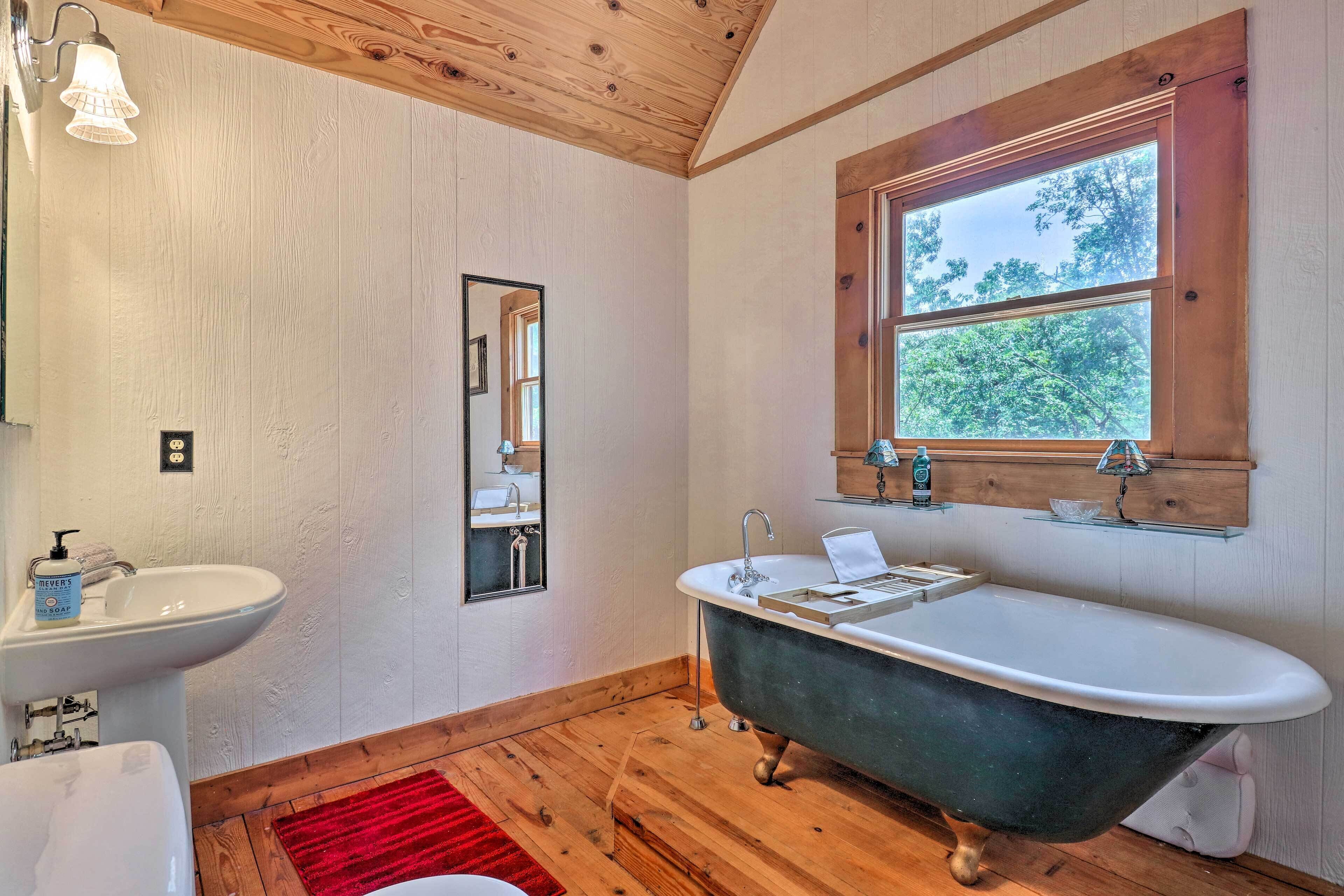 A bathroom with a wooden floor, a white sink, a black bathtub, and a window with a view of trees.