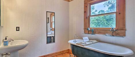 A bathroom with a wooden floor, a white sink, a black bathtub, and a window with a view of trees.