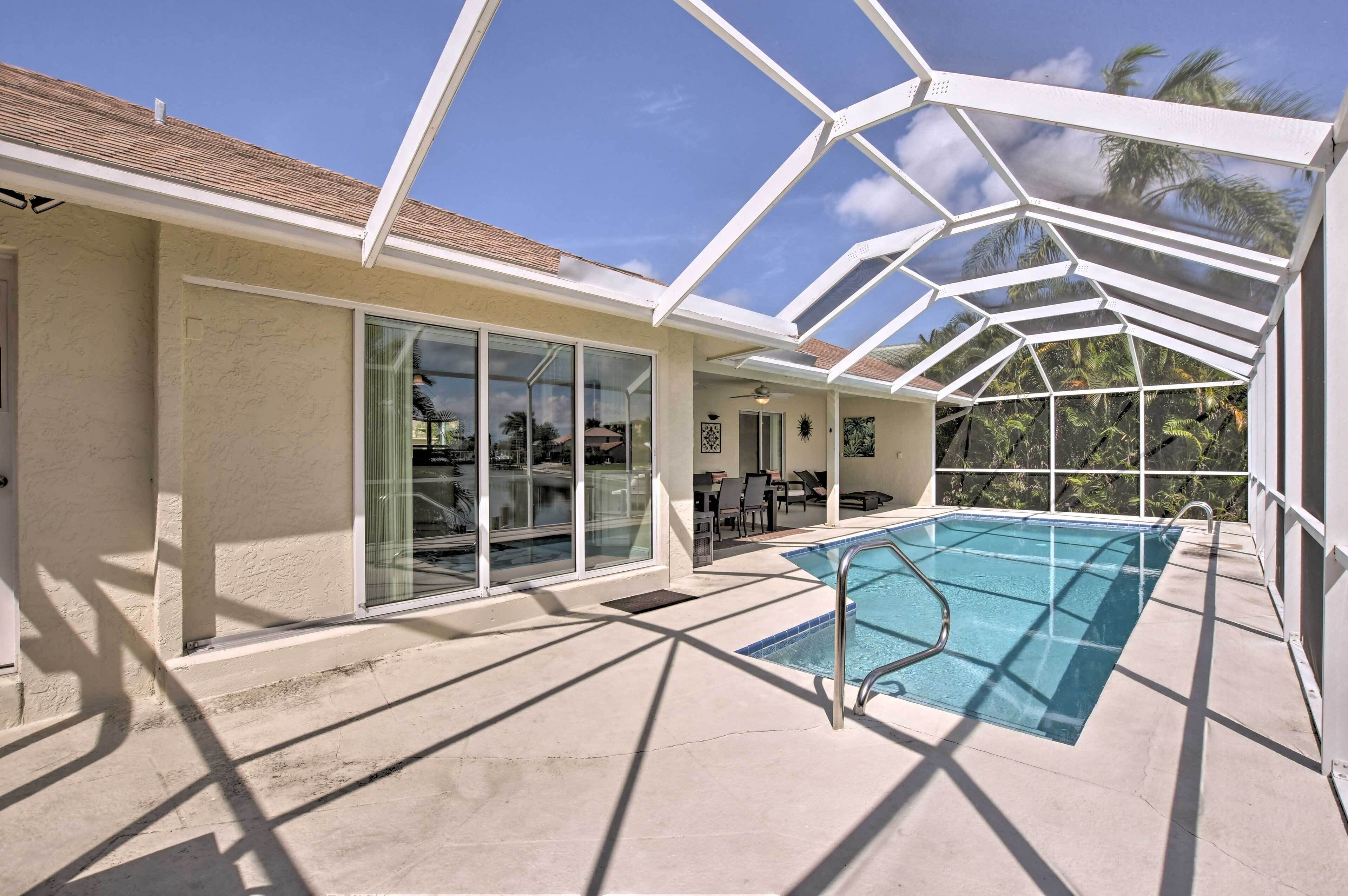 A covered outdoor swimming pool with a glass enclosure, adjacent to a building with large windows and a door.