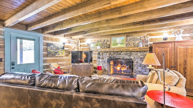 A rustic interior with a stone fireplace, leather sofa, and wooden beams. - Lovely Flat Rock Cabin From 1905 w/ Fireplace (Flat Rock)
