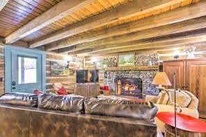 A rustic interior with a stone fireplace, leather sofa, and wooden beams. - Lovely Flat Rock Cabin From 1905 w/ Fireplace (Flat Rock)