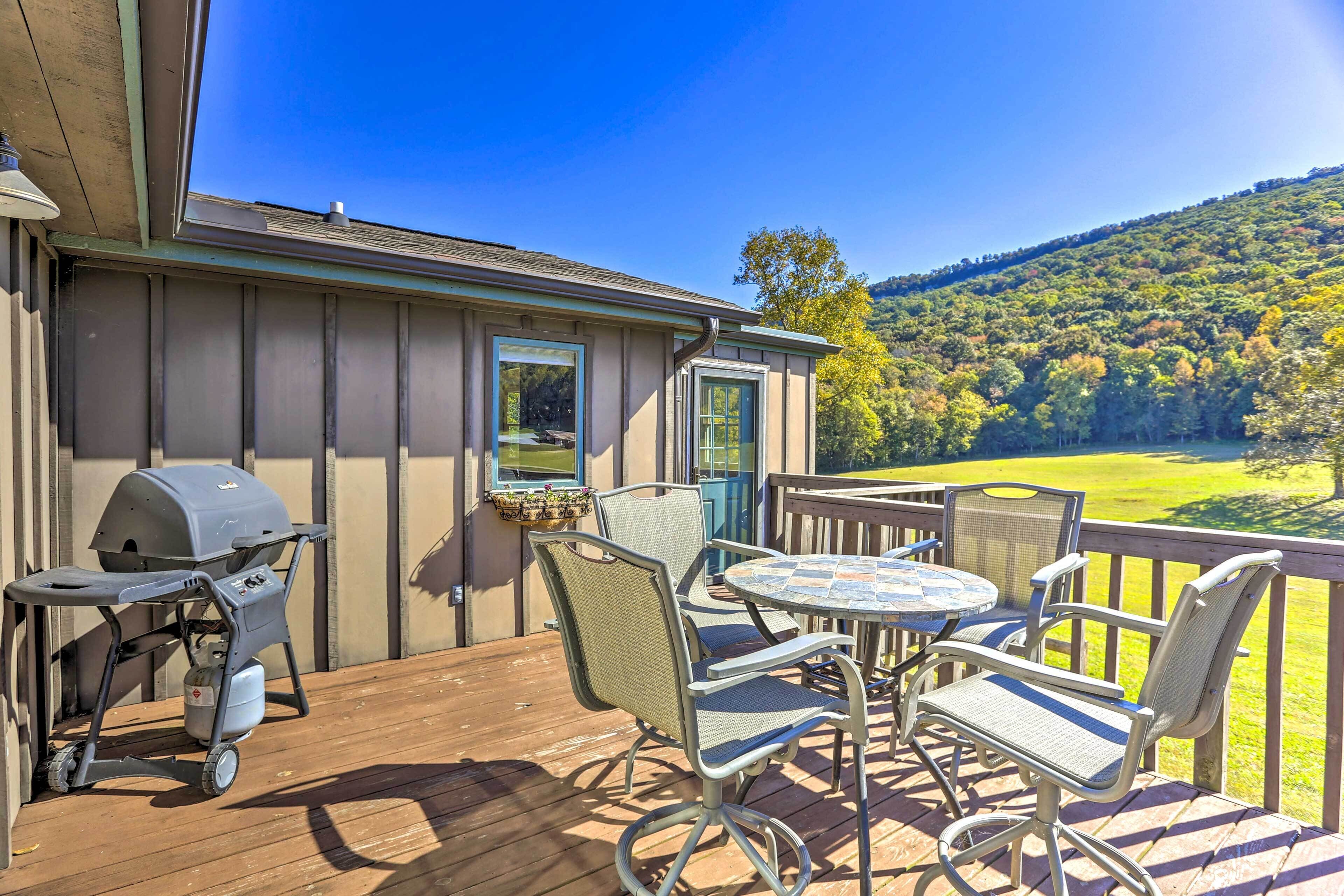 A deck with outdoor furniture, a grill, and a view of a forested hillside.