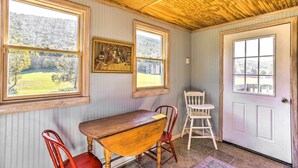 A room with a wooden ceiling, two windows with views of a green landscape, a wooden table, and two chairs. - Lovely Flat Rock Cabin From 1905 w/ Fireplace (Flat Rock)