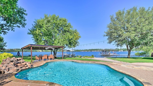 Une piscine dotée d’une pergola et de chaises, entourée d’arbres et offrant une vue sur un lac.