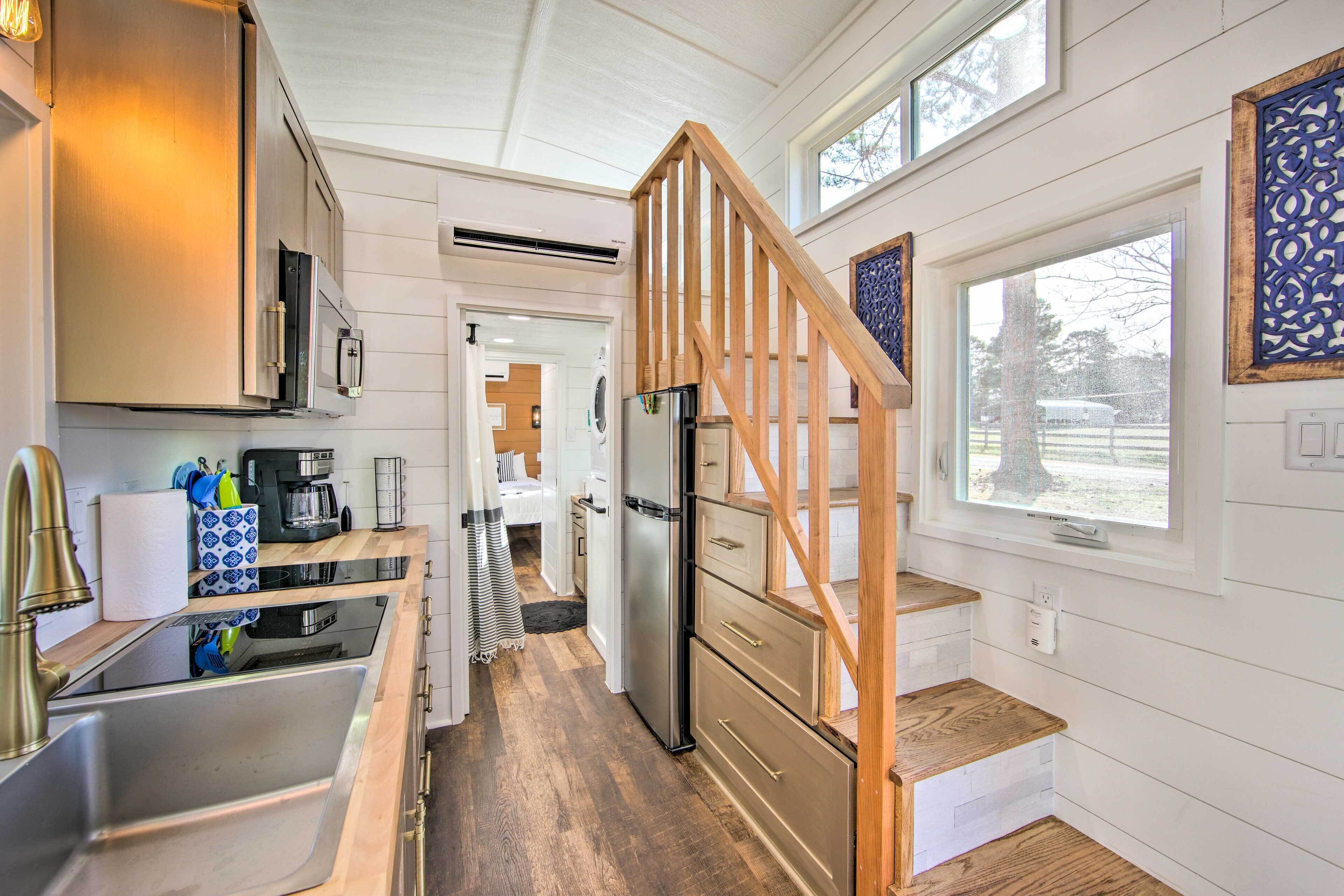 A modern kitchen with a wooden staircase, stainless steel appliances, and a large window.