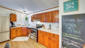 A kitchen with wooden cabinets, a chalkboard with a welcome message, and a sign for 'Fresh Herbs & Dry Goods'.