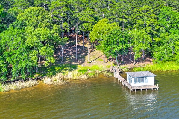 A wooden dock extending into a calm body of water, surrounded by dense green foliage. - Lakefront Crockett Cabin w/ Boathouse & Kayaks! (Grapeland)