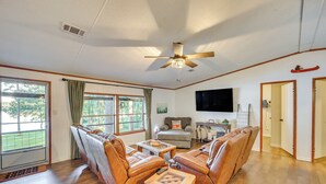 A spacious living room with a ceiling fan, leather sofas, a coffee table, and a television mounted on the wall.