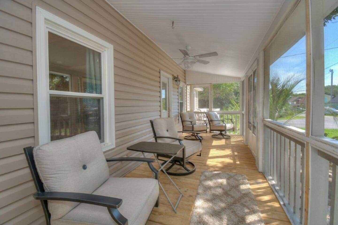 A covered porch with four chairs, a small table, and a ceiling fan.