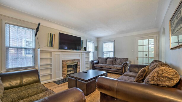 A living room with leather sofas, a fireplace, a flat-screen TV, and large windows. - Dearborn Home w/ Games & Furnished Patio (Dearborn)