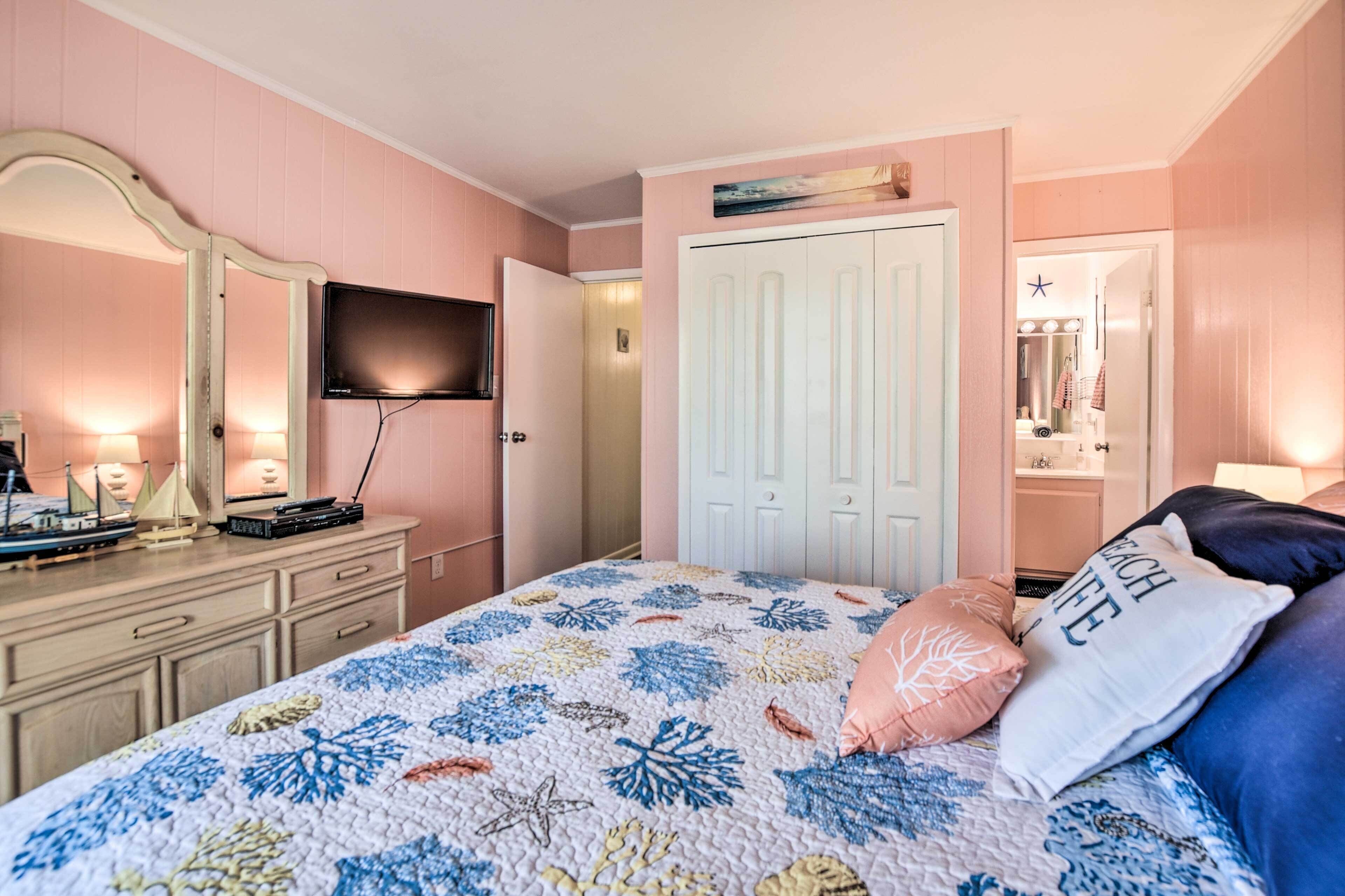 A bedroom with a bed, dresser, TV, and a door leading to another room.