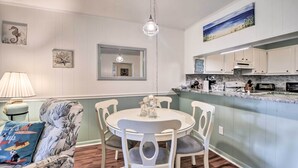 A dining area with a round table and chairs, a hanging light fixture, and a kitchen with white cabinets and a marble countertop. - Walk to Ocean: Unit w/ Balconies in Myrtle Beach! (Myrtle Beach)