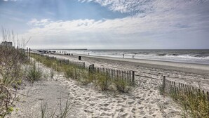 A beach with a wooden fence, sandy dunes, and the ocean. - Walk to Ocean: Unit w/ Balconies in Myrtle Beach! (Myrtle Beach)