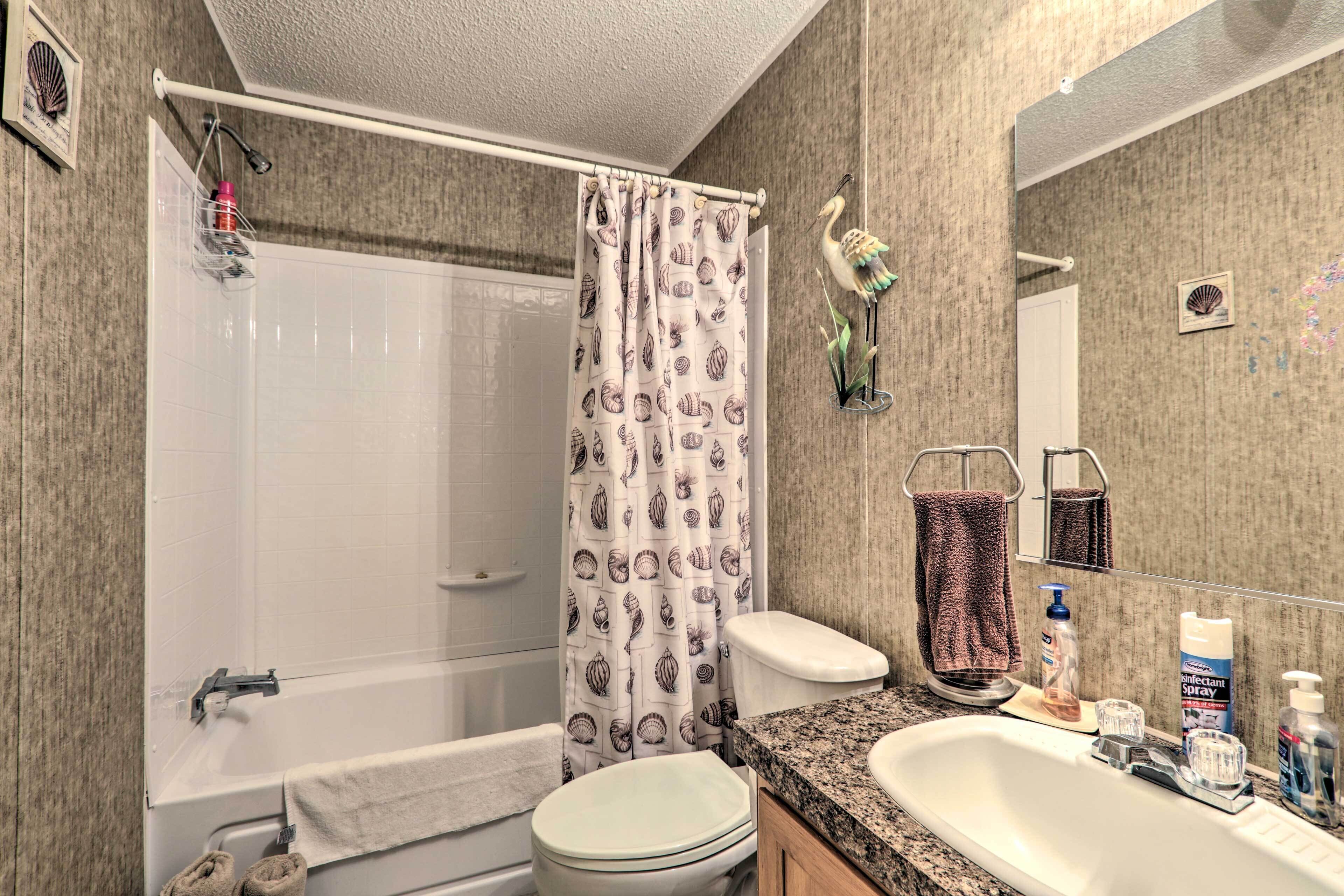 A bathroom with a bathtub, toilet, and sink. There is a shower curtain with a shell pattern, a towel rack, and a mirror.