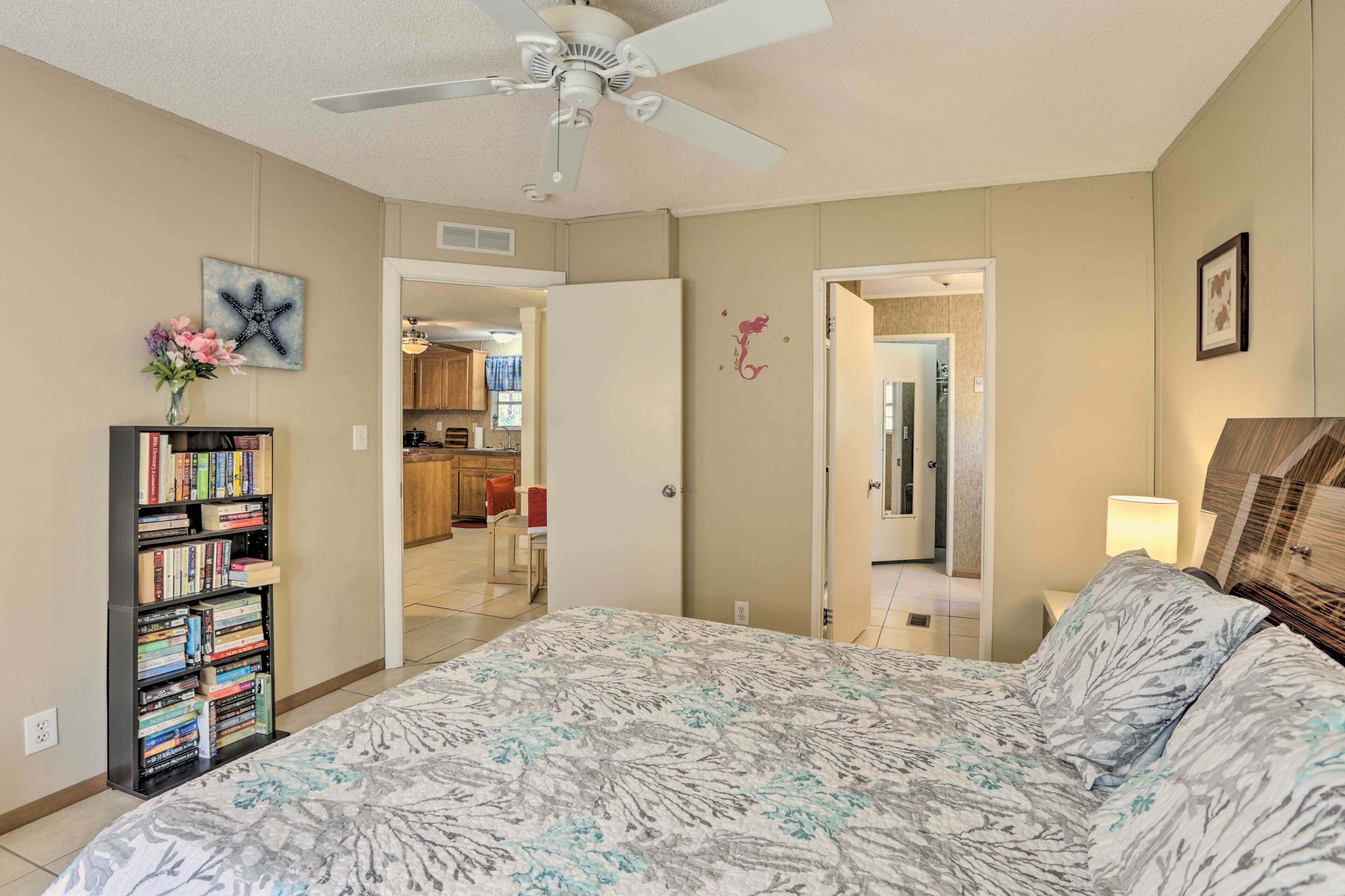 A bedroom with a bed, a ceiling fan, a bookshelf, and a door leading to a bathroom.