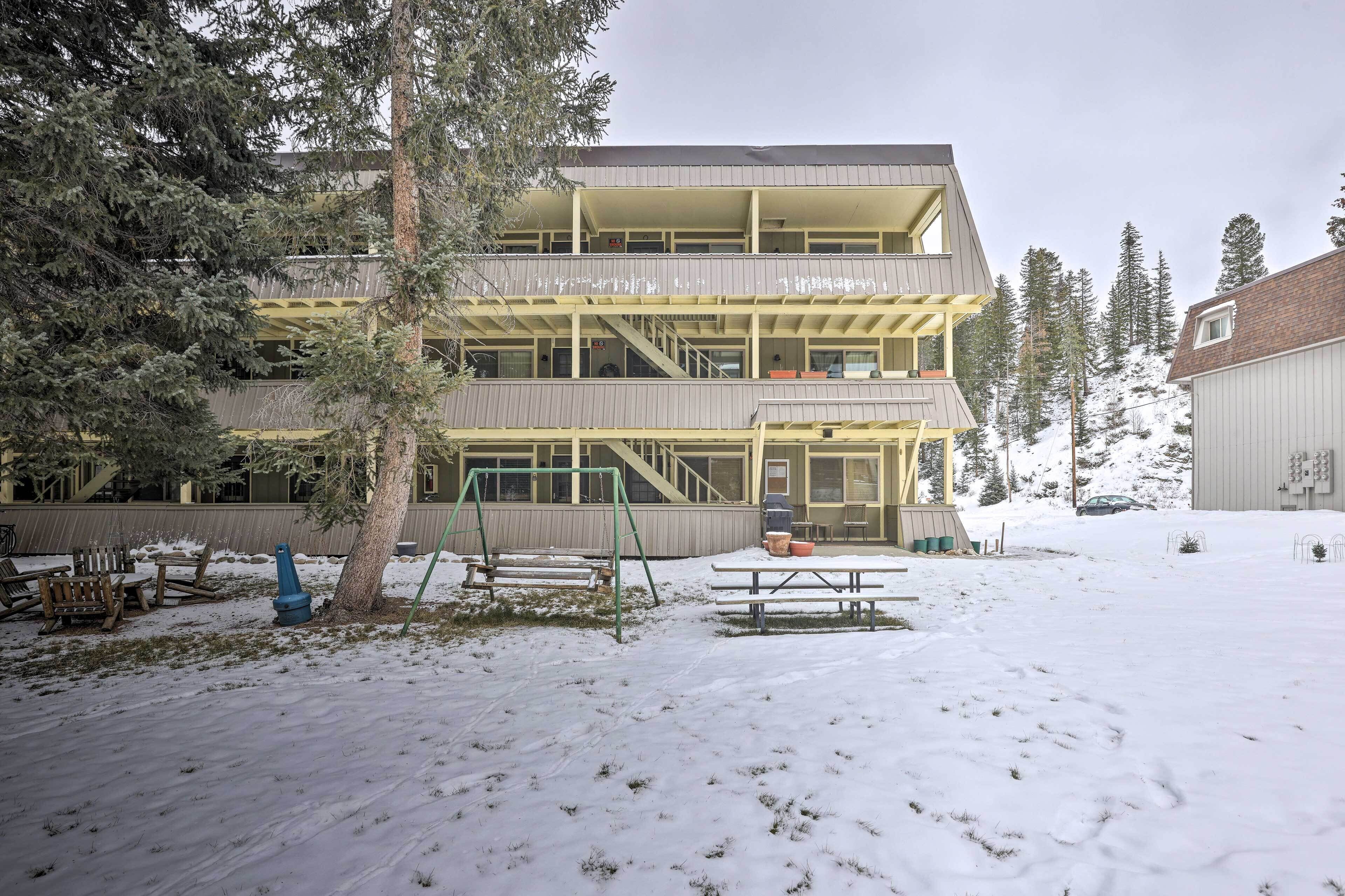 A multi-story building with a flat roof, surrounded by snow-covered ground and trees.