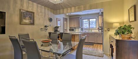 A modern kitchen with stainless steel appliances, a dining area with a glass table and chairs, and a view of the mountains through the window.