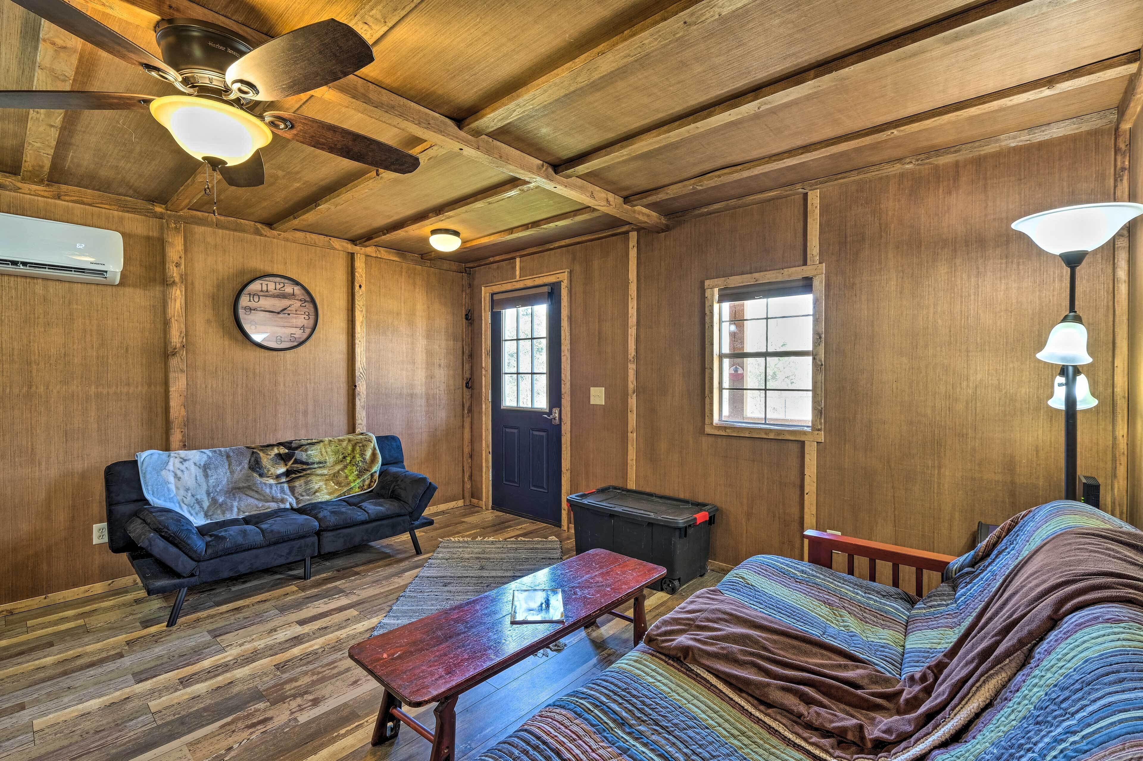 A wooden interior with a ceiling fan, a clock, a sofa, a table, and a lamp.