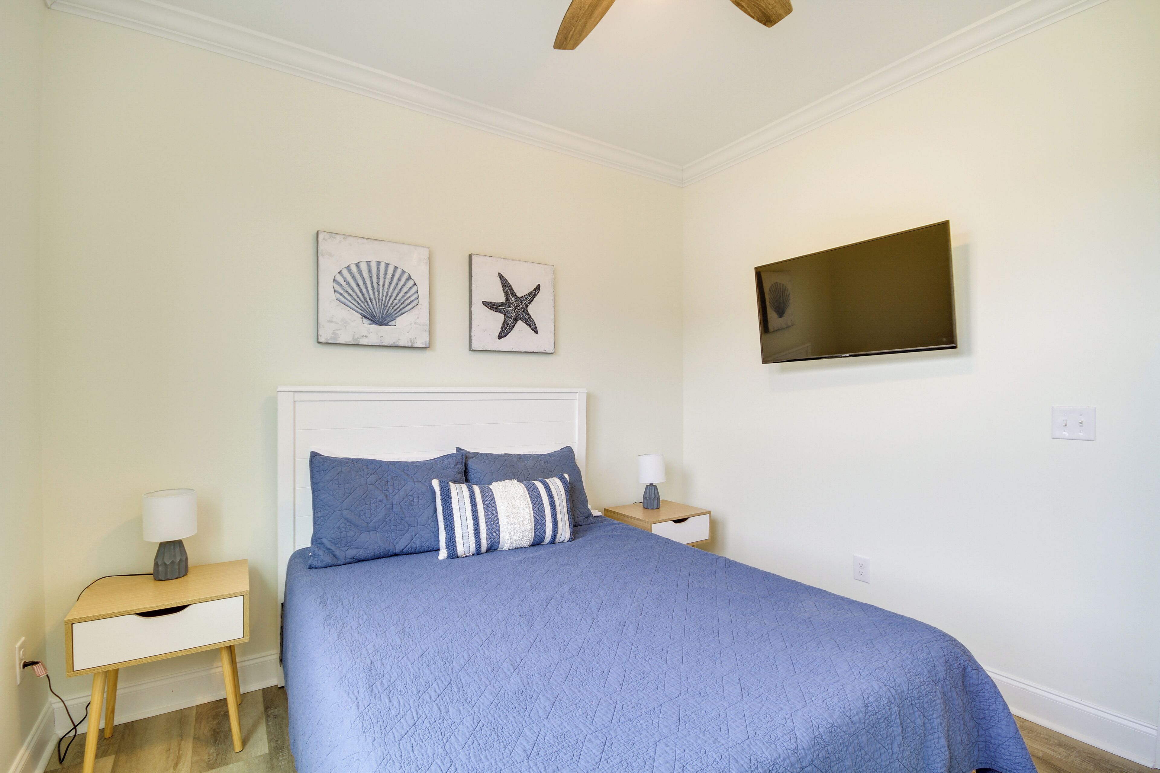 A bedroom with a bed, two nightstands, a flat-screen TV, and wall art.