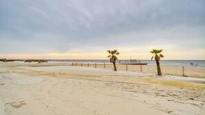 Ein sandiger Strand mit zwei Palmen und einer Holzpromenade, die zum Wasser führt.