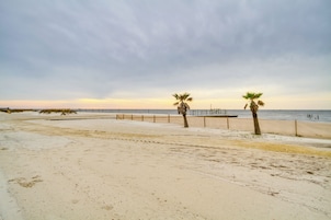 Una playa arenosa con dos palmeras y un camino de madera que conduce al agua.