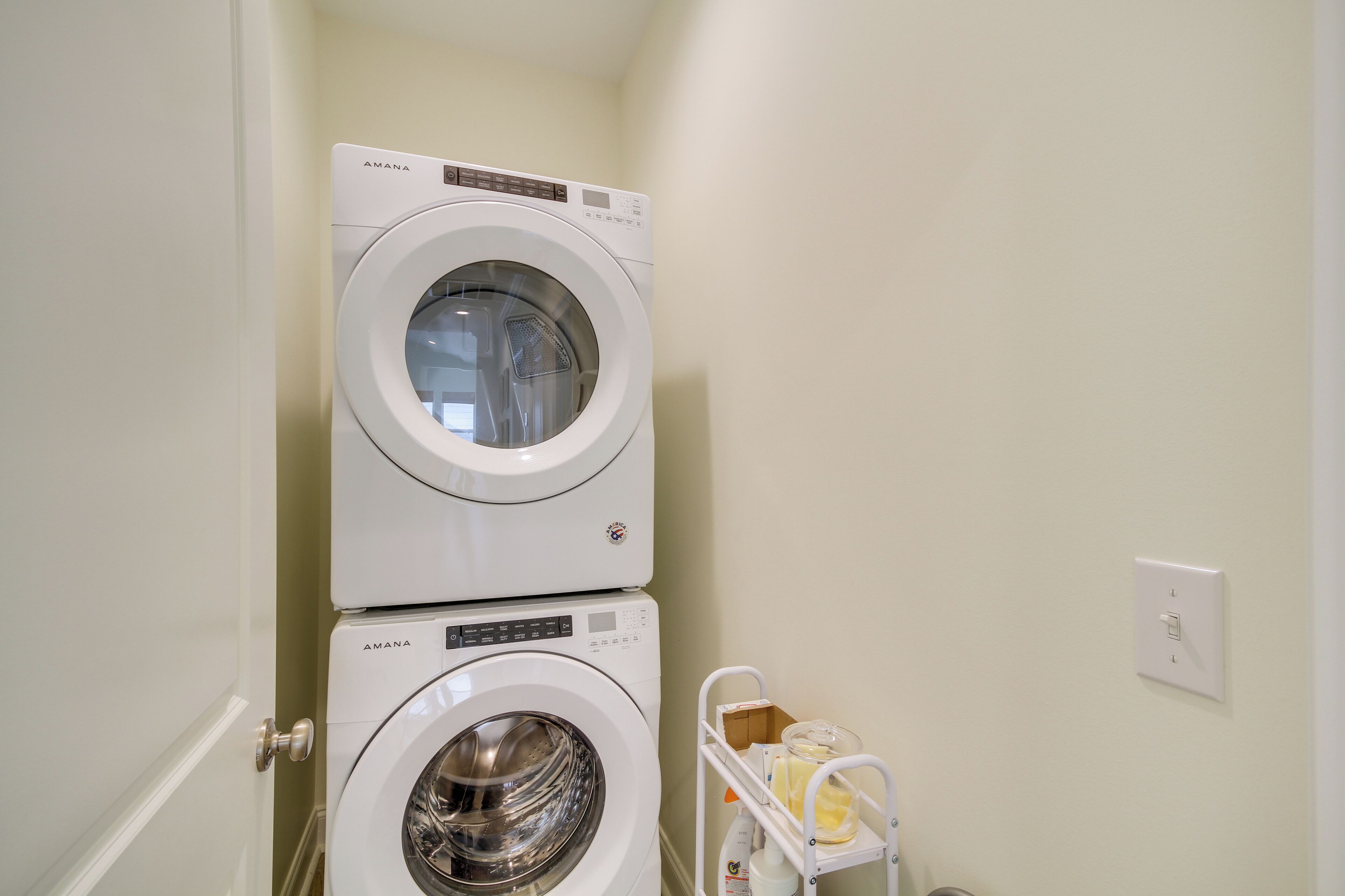 Een wasruimte met twee gestapelde wasmachines en een klein karretje met schoonmaakspullen.