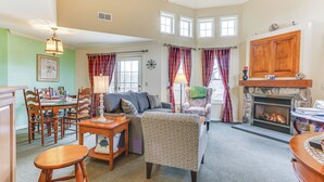 A cozy living room with a fireplace, a dining area with wooden furniture, and a view of the outside through large windows. - Spacious Condo w/ View < 1 Mi to Mtn Creek Resort! (Vernon)