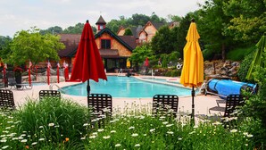 A pool area with lounge chairs and umbrellas, surrounded by greenery and a building with a red roof. - Spacious Condo w/ View < 1 Mi to Mtn Creek Resort! (Vernon)