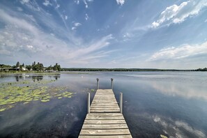 Muelles de madera que se adentran en aguas tranquilas con nenúfares, rodeado de árboles y un cielo despejado.