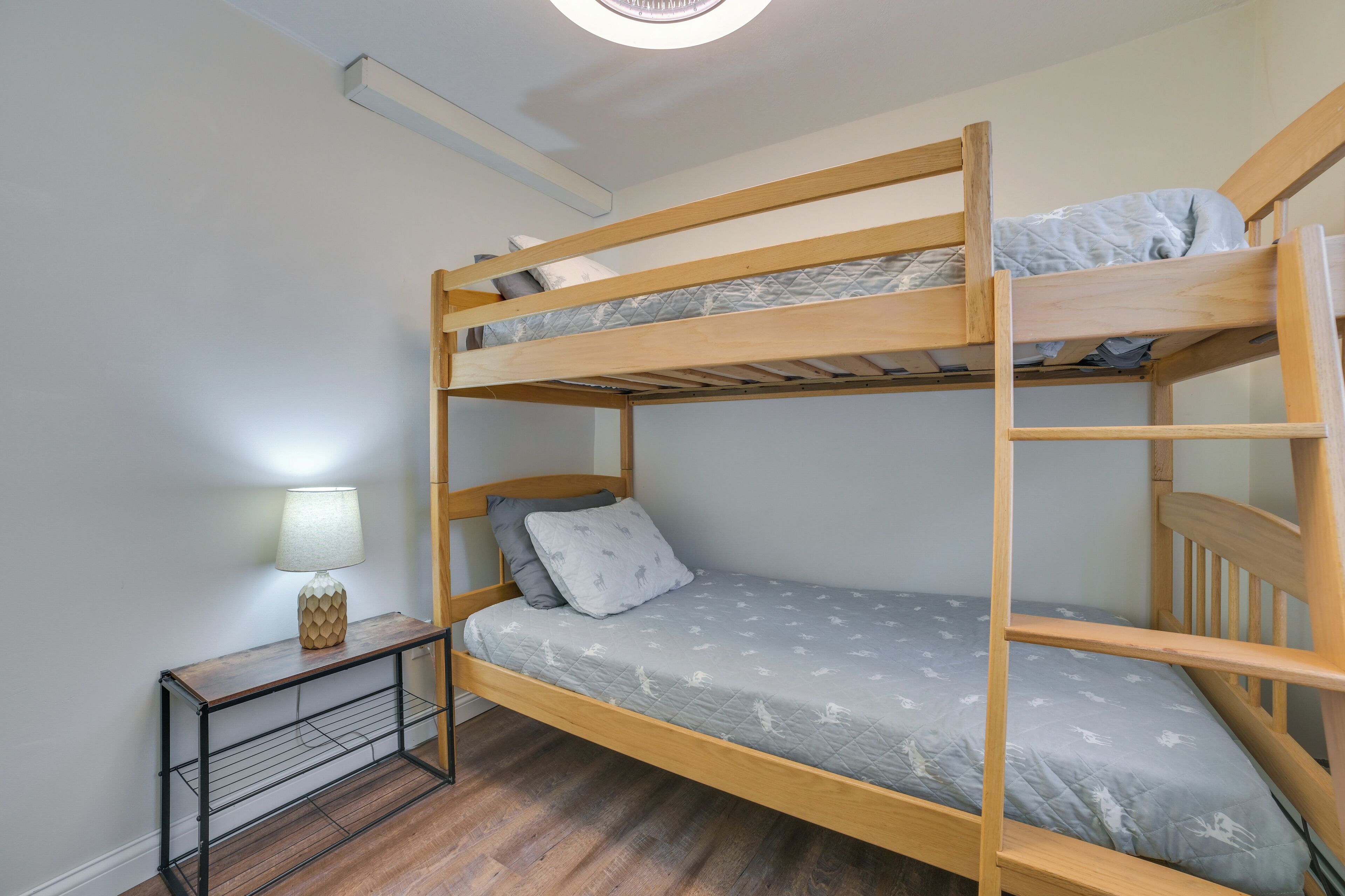 A bunk bed room with a wooden frame, a nightstand with a lamp, and a patterned bedspread.