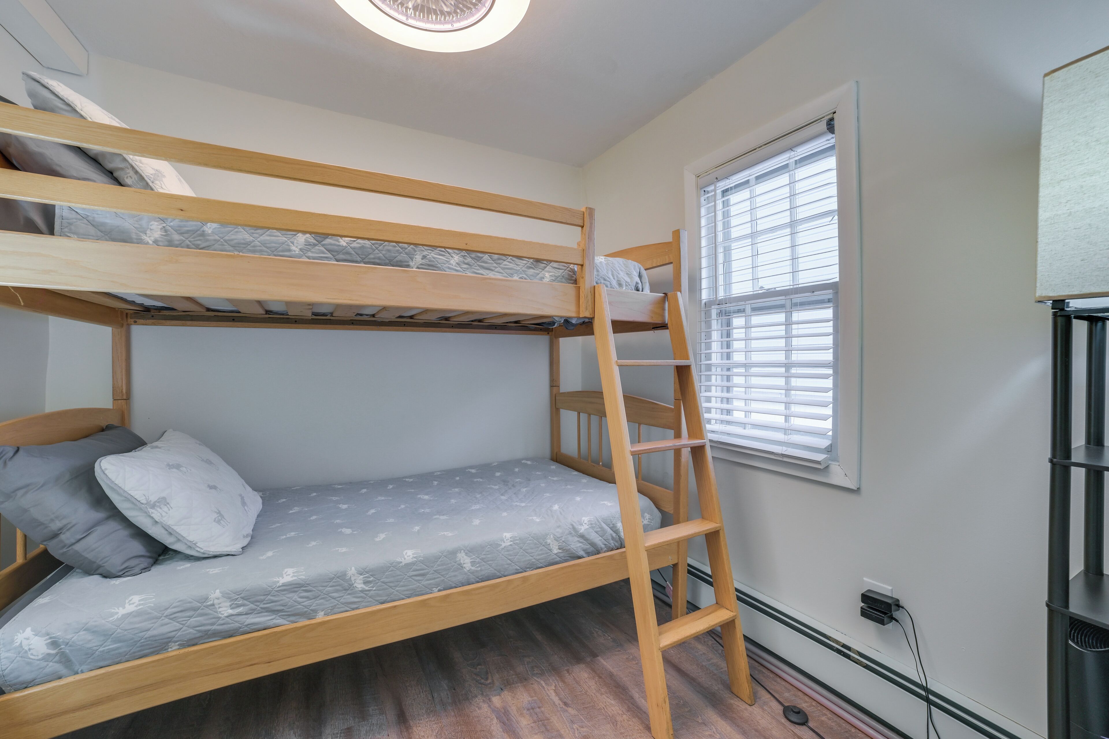 Une chambre avec un lit superposé, une échelle, une fenêtre avec des stores et une prise électrique au mur.