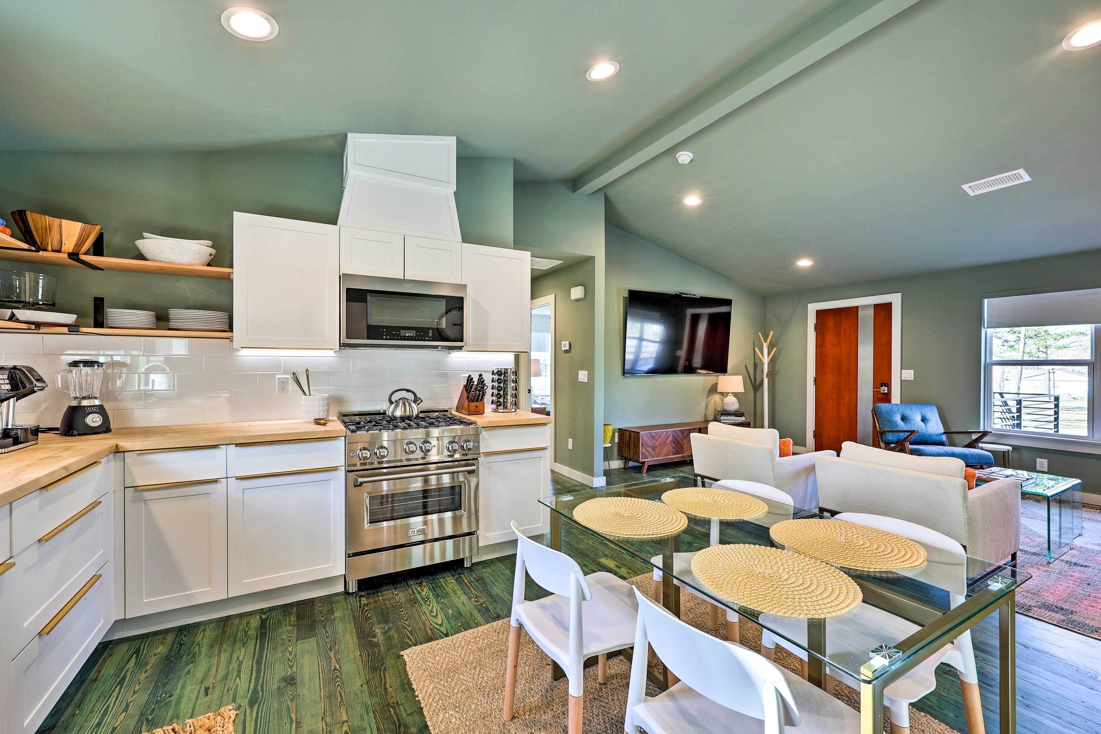 A modern kitchen with white cabinets, stainless steel appliances, and a dining area with glass tables and white chairs.