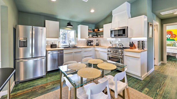 Una cocina moderna con electrodomésticos de acero inoxidable, una mesa de comedor de vidrio y armarios blancos.