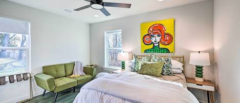 Un dormitorio con una cama, un sofá verde, un ventilador de techo, una ventana y un cuadro en la pared.