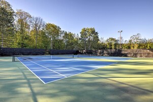 Cancha de tenis con una red, rodeada de árboles y un muro de piedra.