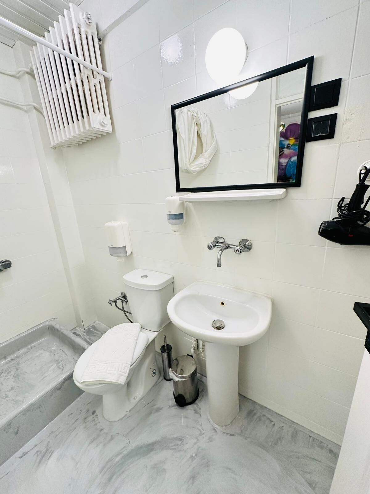 A bathroom with a white toilet, a sink, a mirror, a towel rack, and a shower area.