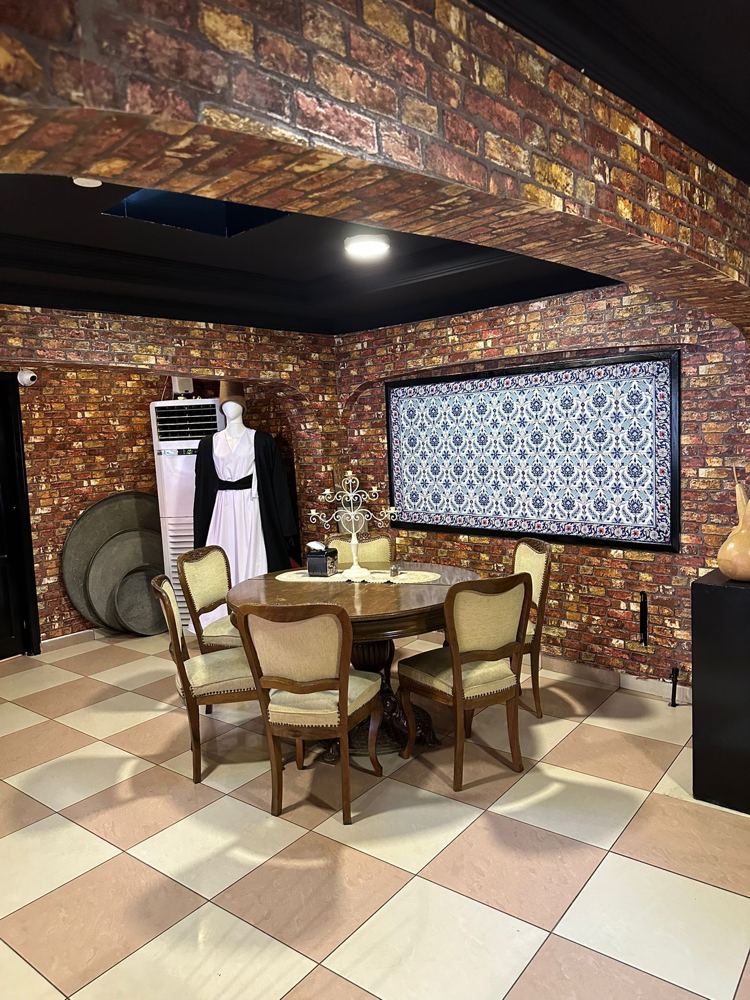Een eetgedeelte met een bakstenen muur, een wanddecoratie met patroon en een etalagepop gekleed in wit en zwart.