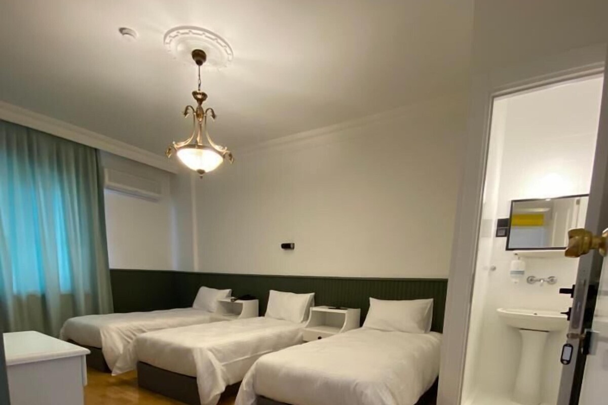 A hotel room with two beds, a small desk, a bathroom with a sink, and a ceiling light fixture.